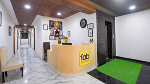 A hotel reception area with a wooden reception desk, a clock, framed pictures, and a marble floor. - Fabhotel Yatri Inn (Noida)