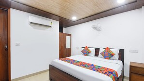 A bedroom with a bed, a wooden door, an air conditioning unit, a bedside table, and a wall-mounted fan. - Fabhotel Yatri Inn (Noida)