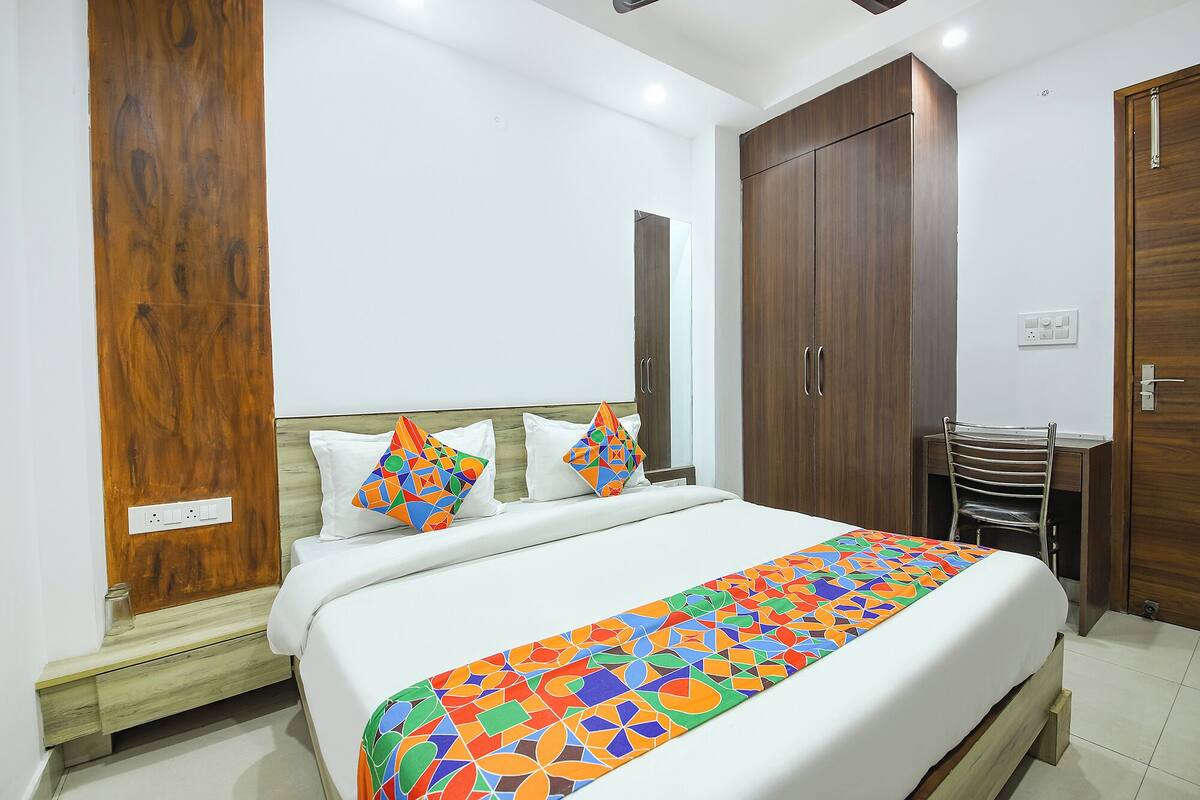 A hotel room with a bed, wooden wardrobe, and a desk with a chair.