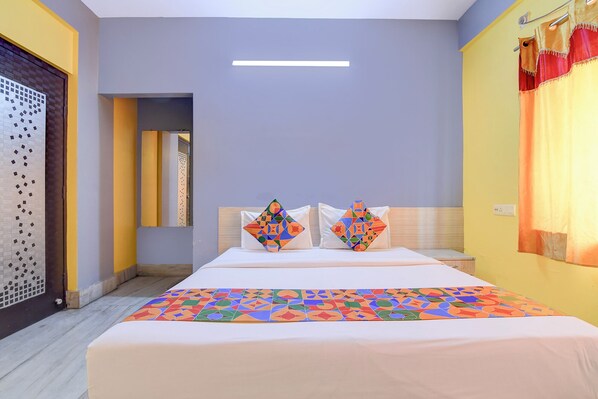 A hotel room with a bed, two pillows, a window with curtains, and a door with a patterned design.