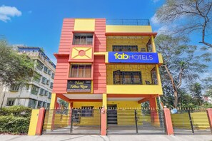 A hotel with a yellow and red facade, a sign for 'fabHOTELS', and a 'Hotel Yellow Rose' sign indicating a premium room with air conditioning and a king-size bed.