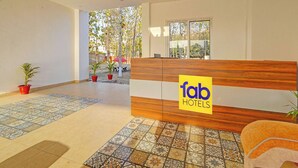 Un espace d’accueil d’hôtel avec un comptoir en bois, un sol carrelé et des plantes en pot.