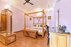 Un lit à baldaquin avec une tête de lit en bois, une table basse en verre, un banc en bois et une commode avec un miroir.