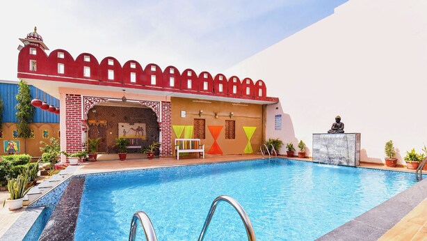 A swimming pool with a red-roofed structure, a Buddha statue, and potted plants. - Fabhotel Nimabal Dhani (Jaipur)