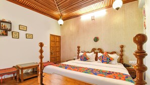 A wooden bed with a headboard, a bedside table, a small bench, and a wall with framed pictures. - Fabhotel Nimabal Dhani (Jaipur)