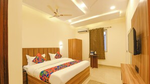 A hotel room with a bed, a ceiling fan, a TV, a wardrobe, and a window with curtains. - Fabhotel Pvs Grand (New Delhi)