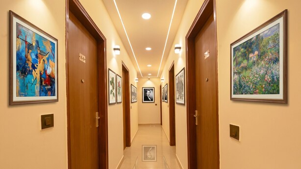 A hallway with framed artwork on the walls, wooden doors, and recessed lighting. - Fabhotel Pvs Grand (New Delhi)
