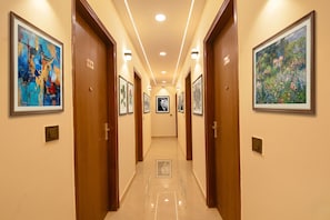 A hallway with framed artwork on the walls, wooden doors, and recessed lighting. - Fabhotel Pvs Grand (New Delhi)