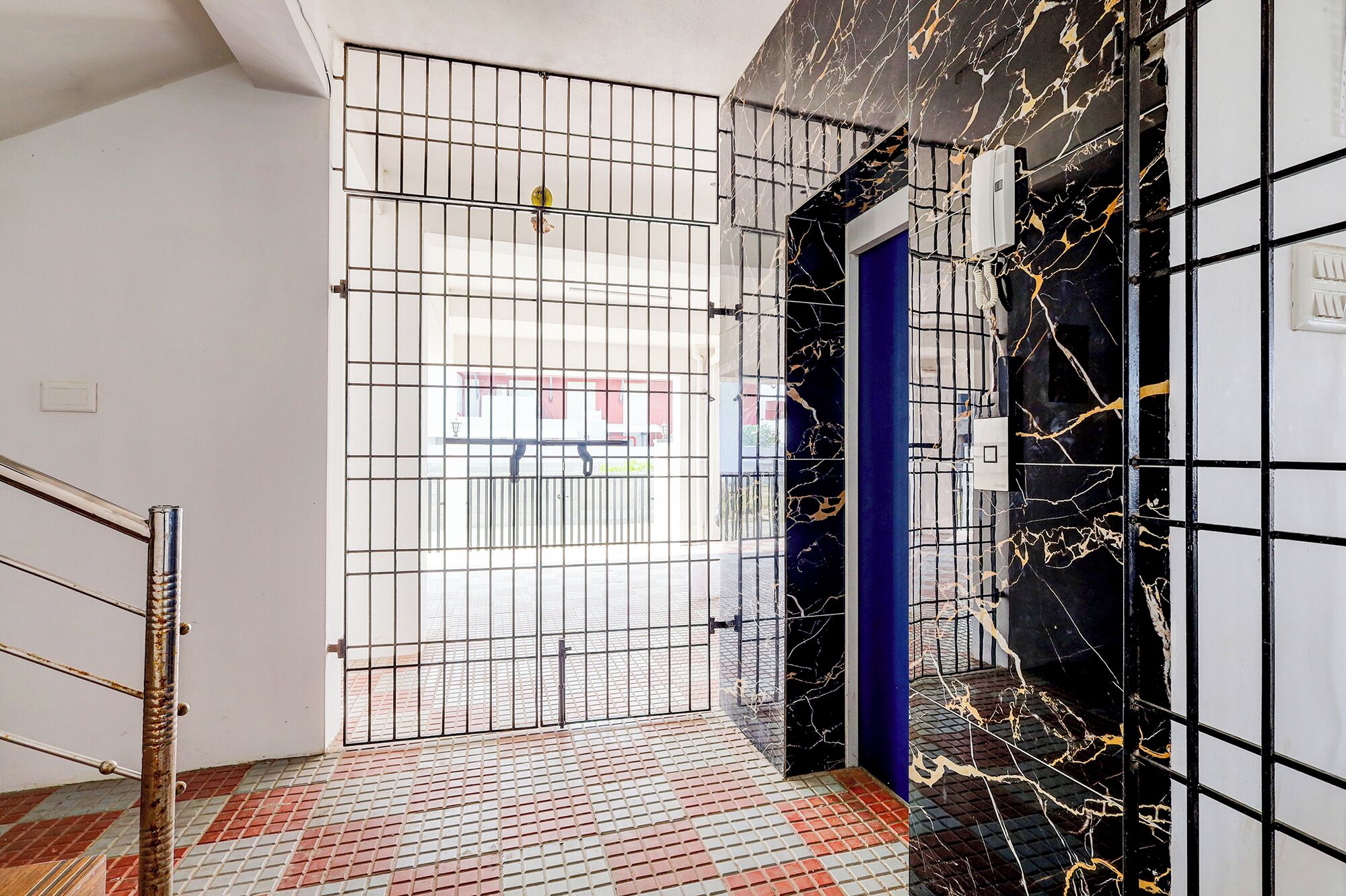 A hallway with a metal gate, a blue door, and a black marble wall with gold veins.