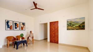 Un hall d’entrée spacieux, doté d’un ventilateur de plafond, d’une porte en bois et d’un tableau représentant un paysage.