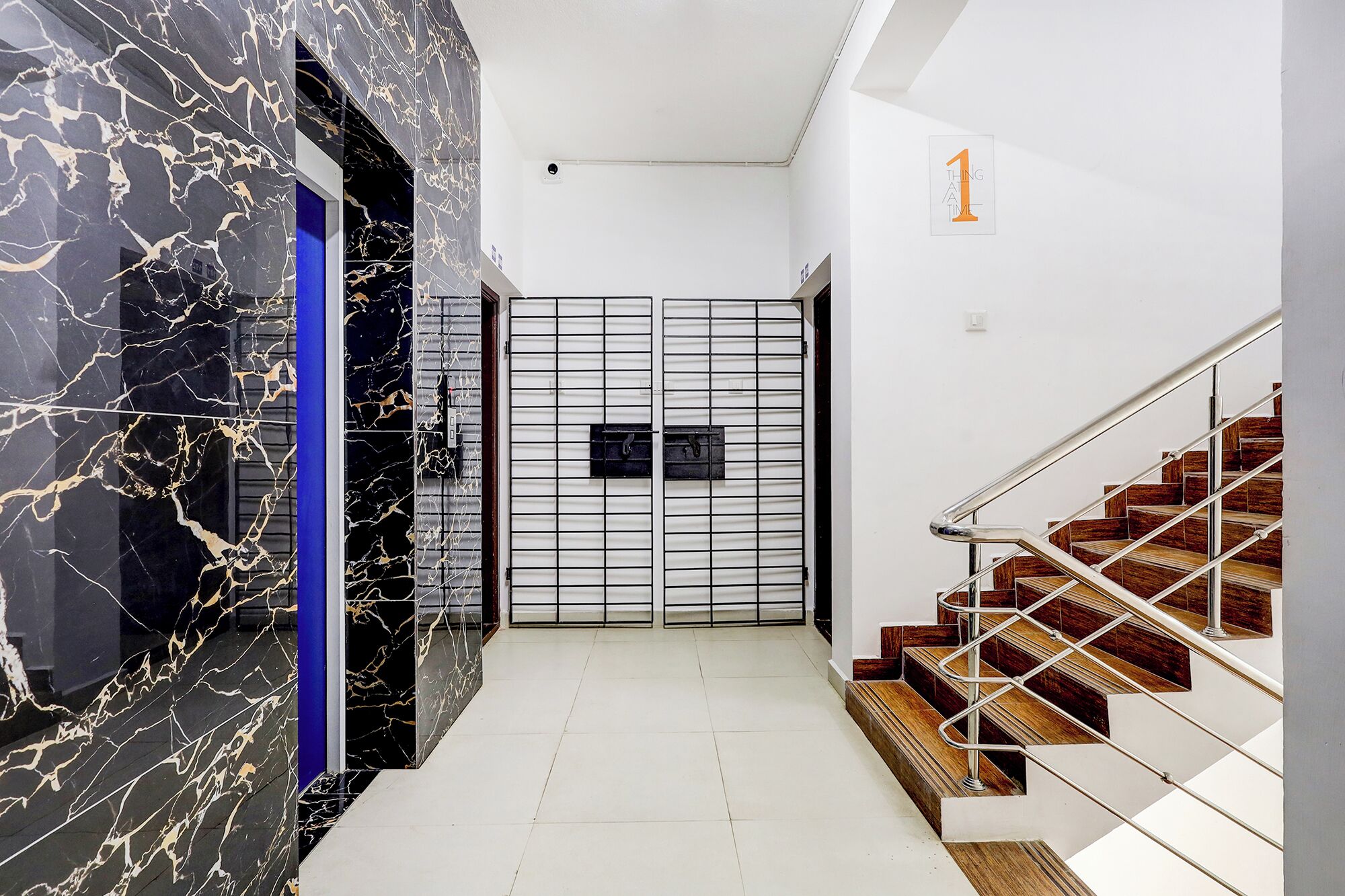 Un couloir avec un mur de marbre, une porte bleue, un portail en métal et un escalier en bois.