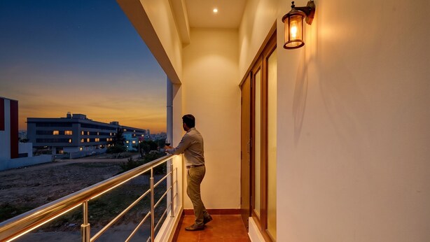 Un homme se tient sur un balcon doté d’une balustrade, et contemple un paysage urbain au crépuscule.