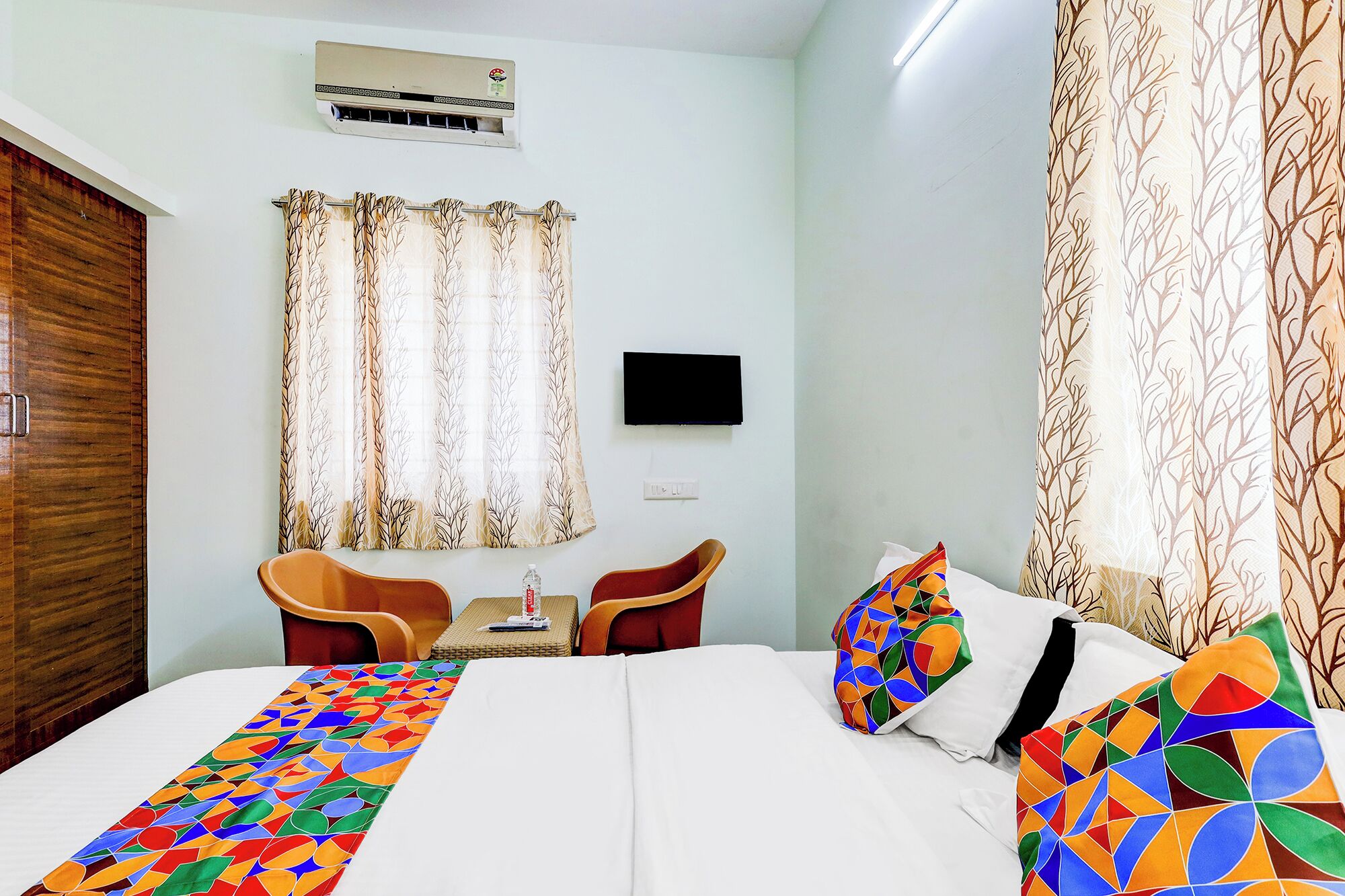 A hotel room with a bed, two chairs, a small table, a TV, and curtains.