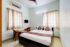 A bedroom with a bed, two chairs, a desk, a flat-screen TV, and a ceiling fan. - Fabhotel Dp Residency (Chennai)