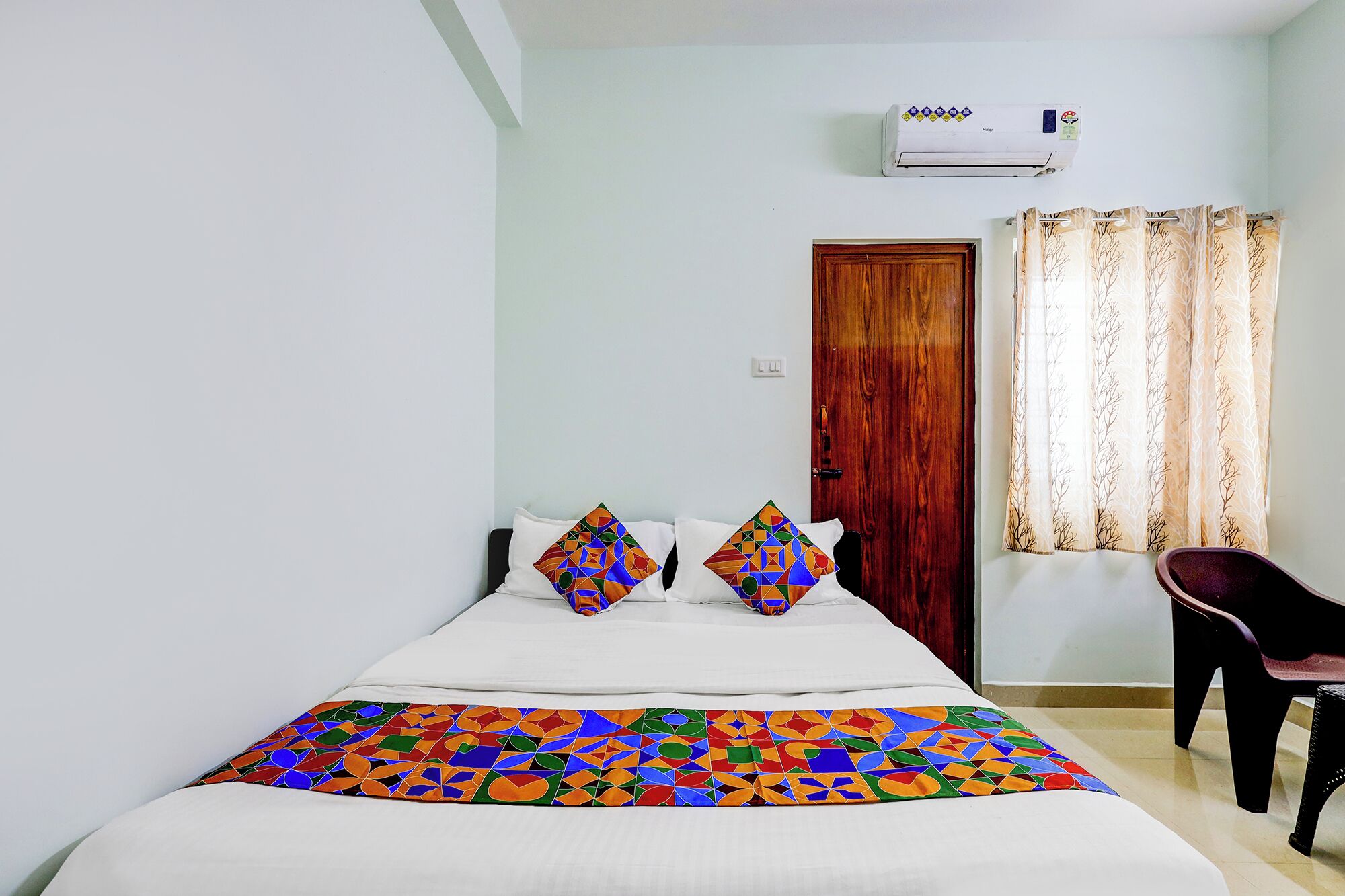 Un dormitorio con una cama, dos almohadas, una silla, una puerta de madera y un equipo de aire acondicionado.