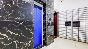 Un couloir aux murs de marbre, un ascenseur bleu et une porte métallique.