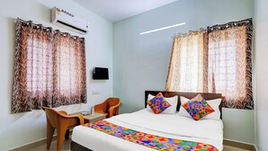 Une chambre d’hôtel avec un lit, deux chaises, une télévision et des rideaux.