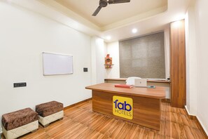 Una recepción de hotel con un letrero de 'fab hotels', una pizarra, un ventanal con cortinas y un ventilador de techo.