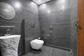 A modern bathroom with a white toilet, a sink with a marble-like backsplash, and a shower area with a handheld showerhead. - Fabhotel Grand Victory (New Delhi)