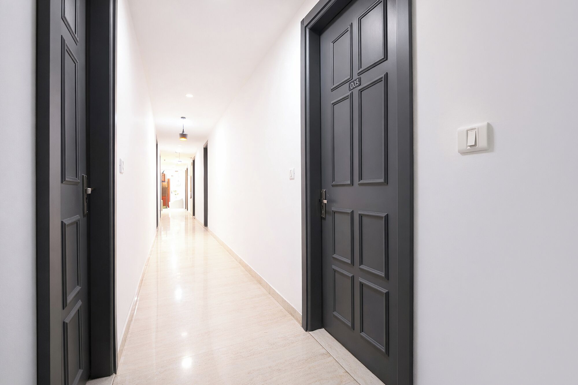 A hallway with dark doors and light walls, leading to a bright room at the end.