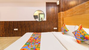 Ett hotellrum med en sänggavel i trä, en rund spegel, en säng med vita sängkläder och färgglada kuddar med geometriska mönster.