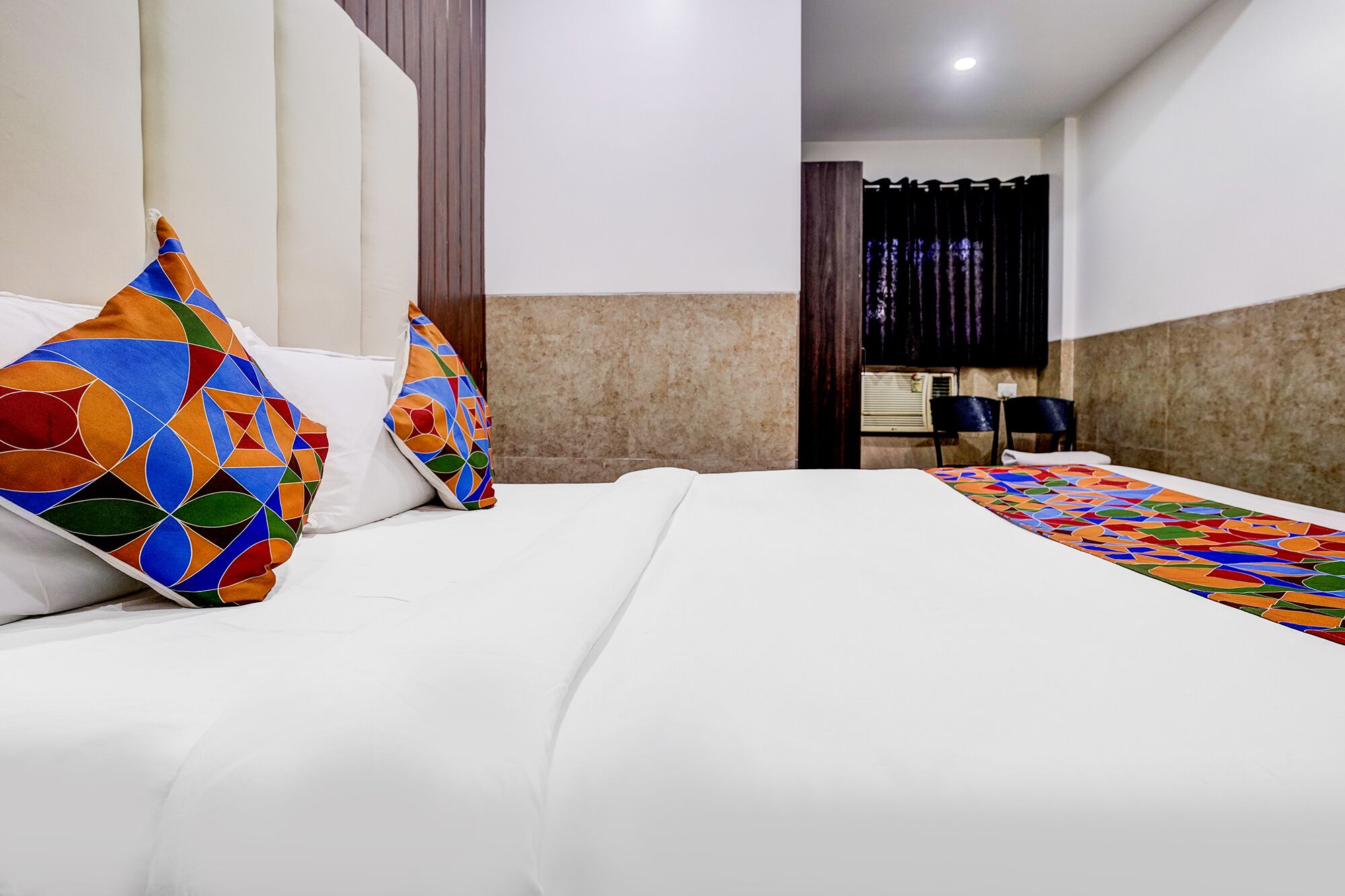 Habitación de hotel con cama, dos almohadas, mesita de noche y una silla.
