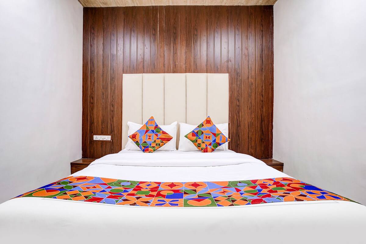 A bed with a colorful geometric-patterned bedspread, two pillows with geometric designs, and a wooden headboard.