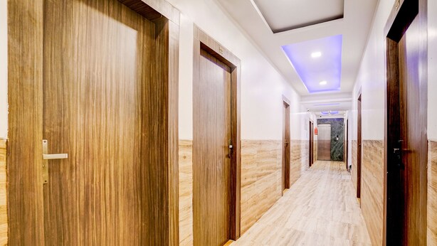 Corredor de hotel com portas de madeira, chão de mármore e teto com iluminação embutida.