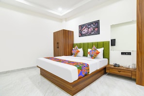 A modern bedroom with a bed, green headboard, wooden wardrobe, and a painting on the wall. - Fabhotel The Backyard Bowl (Sanwer)