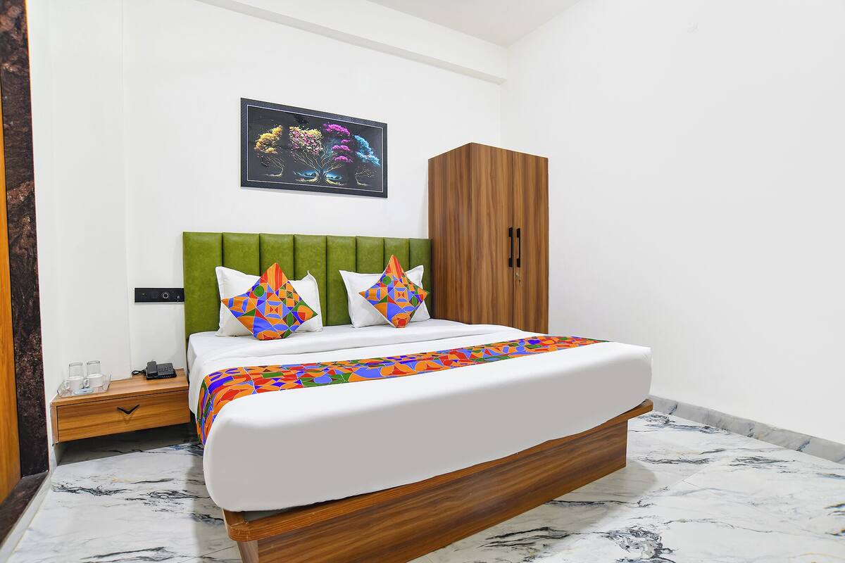 Una cama con cabecera verde, dos almohadas con diseños geométricos, un armario de madera y un suelo de mármol.