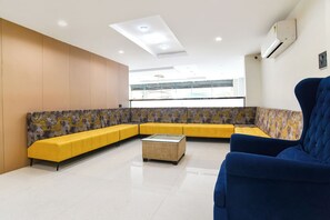 Un'area d'attesa moderna con un divano giallo, una poltrona blu e un tavolino in vetro.