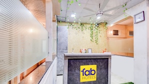 En receptionsdisk med logotypen för ”fab hotels”, ett receptionsområde med en grön vägg och en takfläkt.