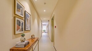 A hallway with framed artwork, a wooden console table with books and a clock, and a potted plant. - Fabhotel Global Stay Rajajinagar (Bangalore)