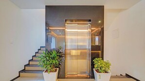 An elevator with a glass door, flanked by two potted plants, and a staircase to the left. - Fabhotel Global Stay Rajajinagar (Bangalore)