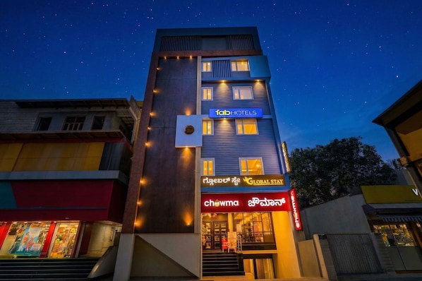 Un edificio de varios pisos con un letrero de 'Tab Hotels', un letrero de 'Global Stay' y un letrero de 'Chowma'.