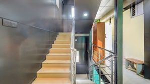 Un escalier avec une rampe en métal, un banc en bois et une porte surmontée d’un rideau vert.