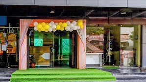 L’entrée d’un hôtel, avec un tapis vert, des portes en verre et une décoration composée de ballons jaunes et blancs.