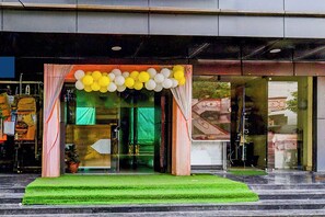 A hotel entrance with a green carpeted entrance, glass doors, and a yellow and white balloon decoration. - Fabhotel Friendly Stay Luxury Room'S (Hyderabad)