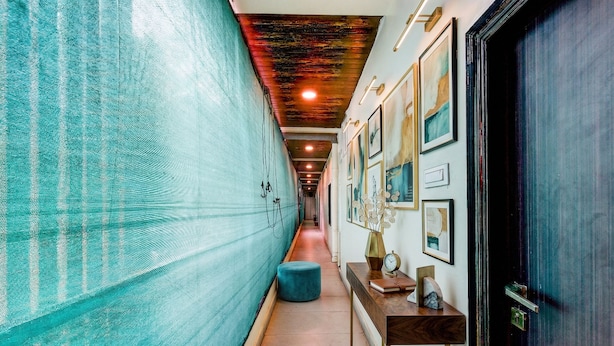 Un couloir avec un mur texturé de couleur turquoise, un pouf rond, une console en bois avec une horloge et des œuvres d’art encadrées accrochées au mur.