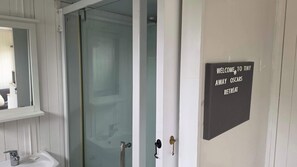 Un bagno con cabina doccia in vetro, un lavandino e un cartello di benvenuto.