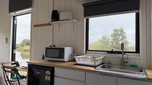 Et lille køkken med mikrobølgeovn, vask og et vindue med udsigt til grønne områder.