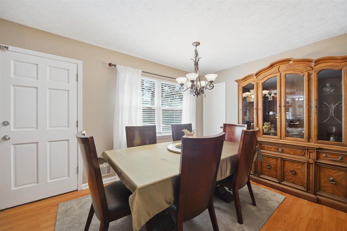 A dining room with a table, chairs, a chandelier, and a wooden cabinet.