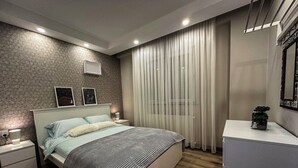 Ein modernes Schlafzimmer mit Bett, Nachttischen, einem Schminktisch und einem Kleiderschrank, sowie einem Fenster mit Vorhängen.