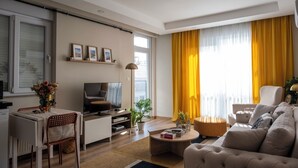 Ein modernes Wohnzimmer mit einer Couch, einem Couchtisch, einem Fernseher und einem Essbereich mit Tisch und Stühlen.