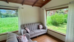 A room with a wooden ceiling, a grey sofa with cushions, and large windows with curtains.