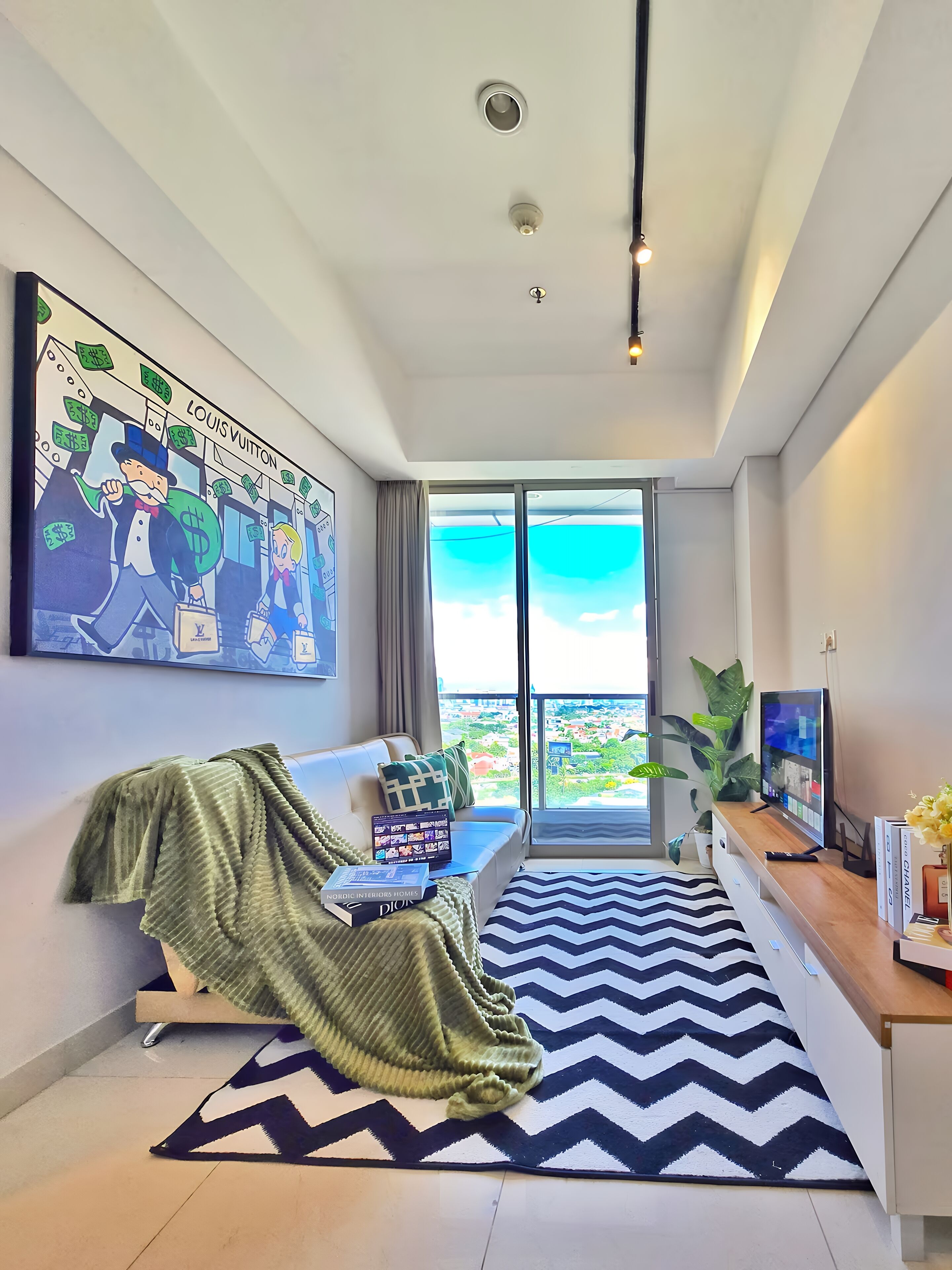 Ein modernes Wohnzimmer mit einem großen Gemälde, einer Couch, einem Couchtisch, einem Fernseher und Blick auf die Stadt.