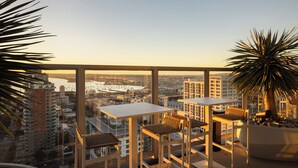 A high-rise balcony with a city view, two tables, and chairs. - Rooftop Pool + Spa + Sky Lounge + Bay Views • Walkable Little Italy | Ancora (San Diego)