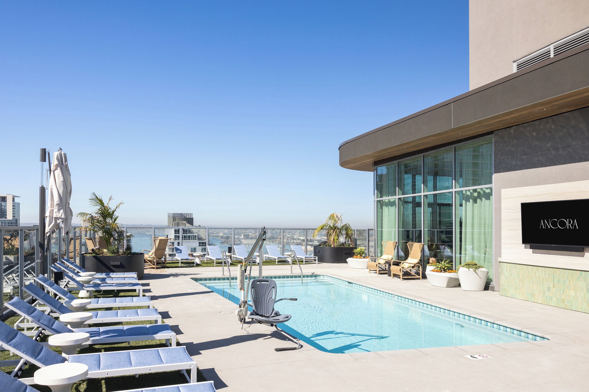 A rooftop pool with lounge chairs, a glass building, and a city view.