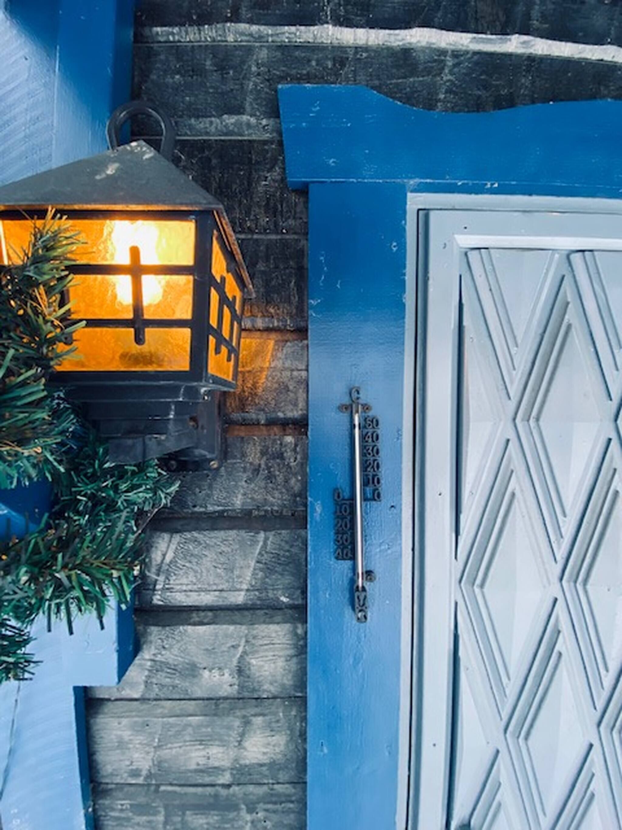 A blue door with a white geometric pattern, a metal handle, and a thermometer indicating 50 degrees.