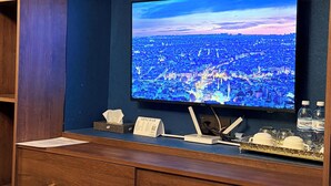 A television displaying a cityscape, a mini bar sign, a tissue box, and a water bottle on a counter. - Gold Perla De Mar Hotel (Baku)